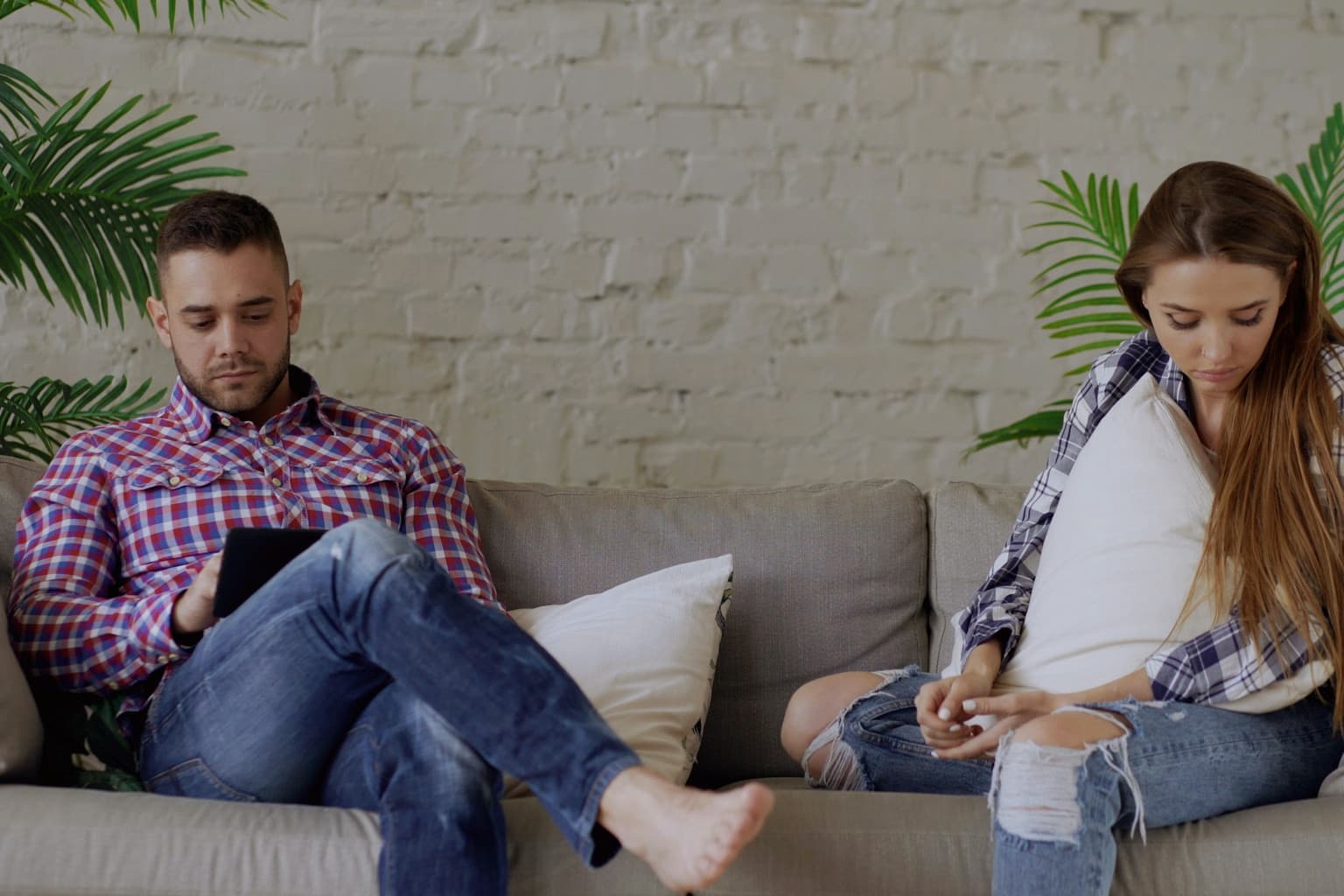 Ein Paar sitzt mit Abstand auf dem Sofa und schaut auf Smartphone und Tablet