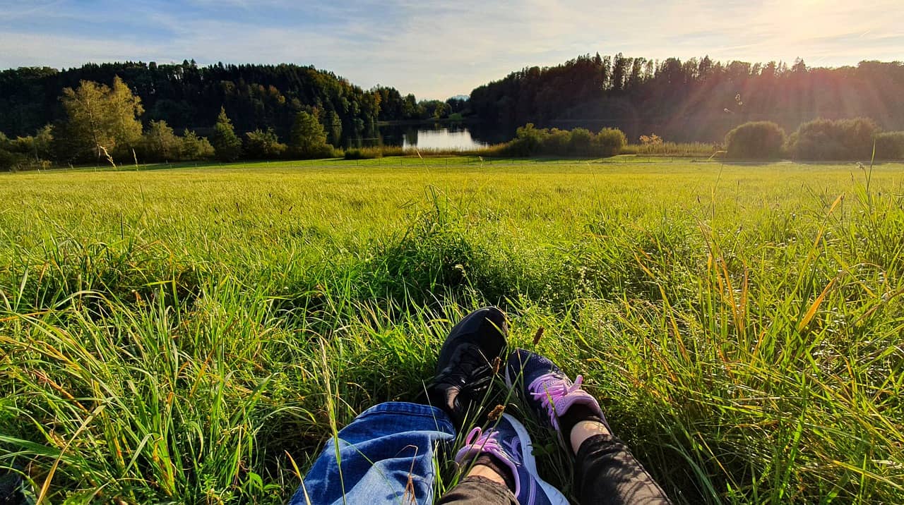 Paar entspannt gemeinsam auf einer Wiese vor See und Wald
