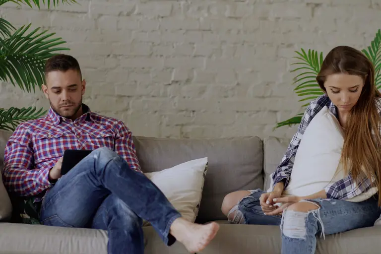 Ein Paar sitzt mit Abstand auf dem Sofa und schaut auf Smartphone und Tablet